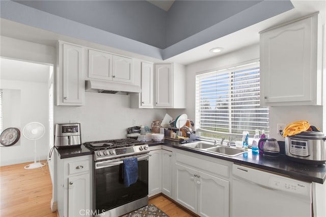 kitchen with stainless steel gas range, white dishwasher, a sink, under cabinet range hood, and dark countertops