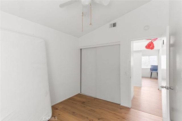 unfurnished bedroom featuring vaulted ceiling, visible vents, a closet, and wood finished floors