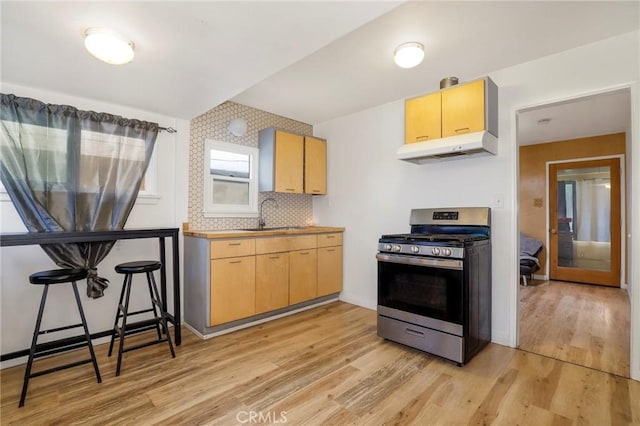 kitchen featuring stainless steel gas range oven, light wood finished floors, under cabinet range hood, decorative backsplash, and a sink