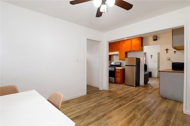 kitchen with a ceiling fan, brown cabinetry, baseboards, light wood-style flooring, and appliances with stainless steel finishes