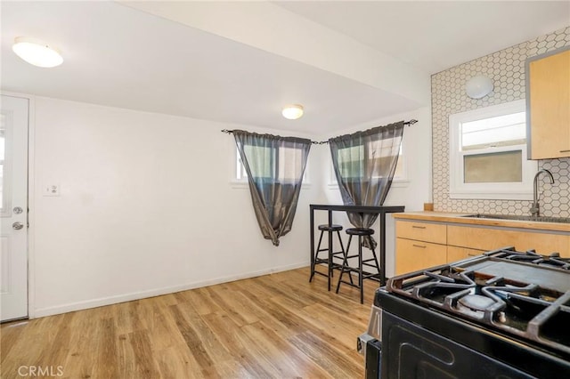 kitchen featuring black gas stove, light wood-style flooring, plenty of natural light, a sink, and backsplash