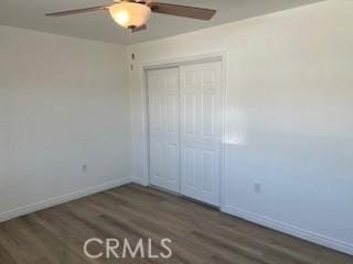 unfurnished bedroom featuring a closet, ceiling fan, baseboards, and wood finished floors