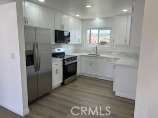 kitchen with light wood-style flooring, a sink, stainless steel appliances, light countertops, and white cabinets