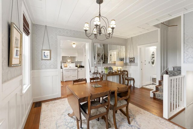 dining space featuring visible vents, stairway, a wainscoted wall, an inviting chandelier, and wood-type flooring