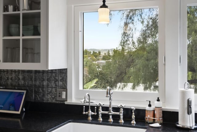 kitchen with a sink, glass insert cabinets, tasteful backsplash, and dark countertops