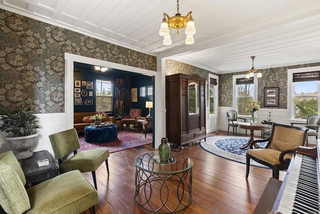 living area with wood-type flooring, an inviting chandelier, wainscoting, and wallpapered walls