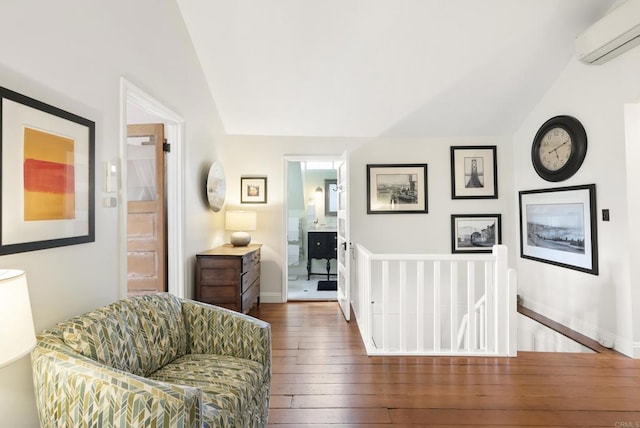 sitting room with an upstairs landing, a wall mounted AC, lofted ceiling, and wood-type flooring