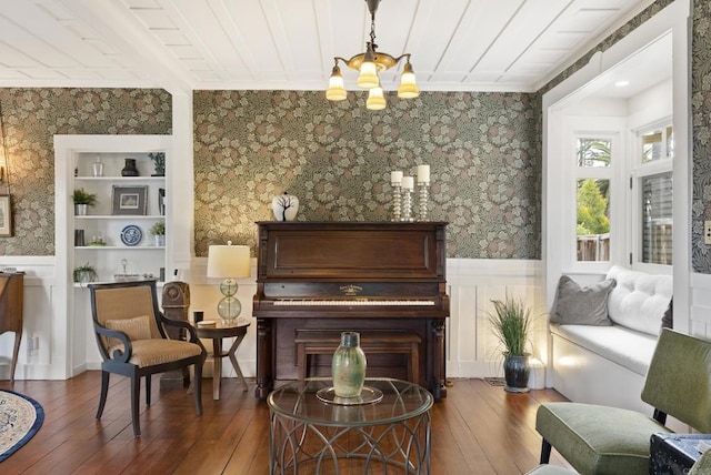 sitting room with wallpapered walls, a chandelier, built in features, wainscoting, and wood-type flooring