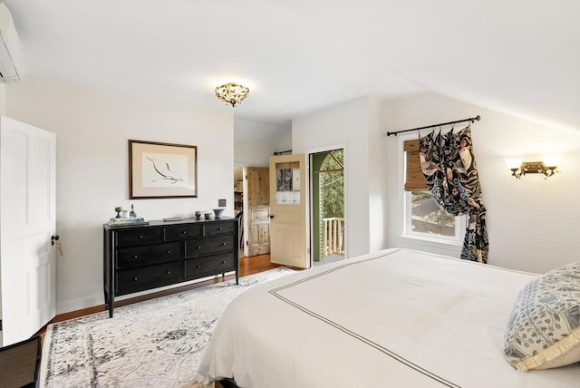 bedroom with a wall unit AC, wood finished floors, baseboards, access to exterior, and vaulted ceiling