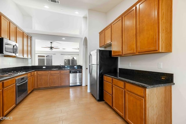 kitchen with brown cabinets, light wood-style flooring, a sink, stainless steel appliances, and arched walkways