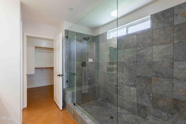 bathroom featuring a walk in closet, baseboards, wood finished floors, and a tile shower