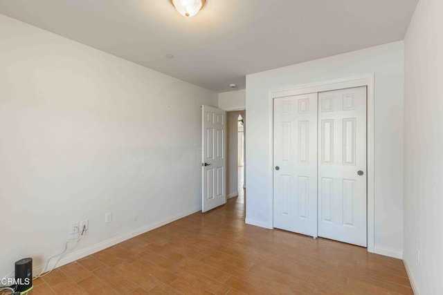 unfurnished bedroom featuring a closet, light wood-type flooring, and baseboards