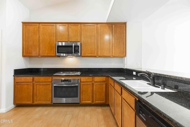 kitchen featuring dark stone counters, light wood-style floors, brown cabinetry, stainless steel appliances, and a sink