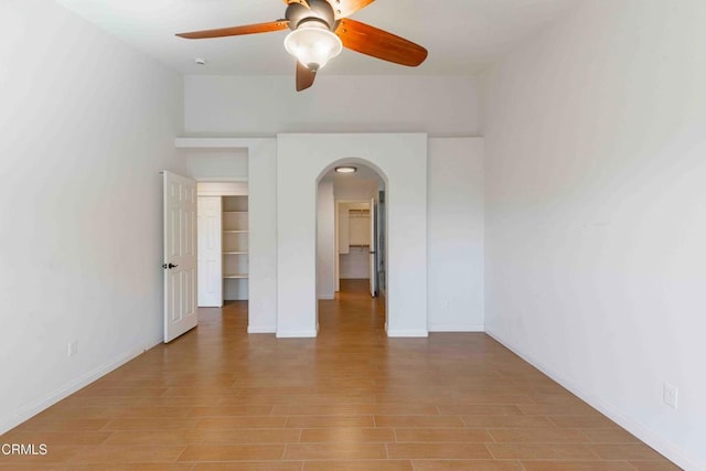 empty room featuring light wood-style flooring, baseboards, arched walkways, and ceiling fan