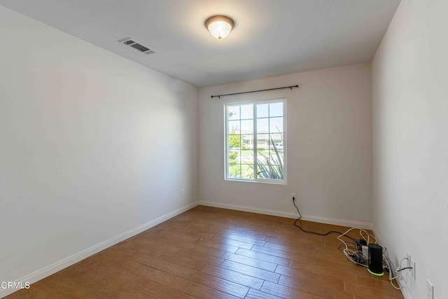 empty room with wood finished floors, visible vents, and baseboards