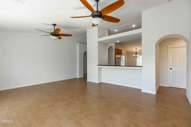 unfurnished living room with wood finished floors, baseboards, recessed lighting, arched walkways, and vaulted ceiling