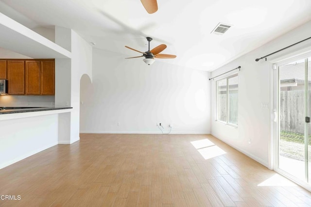 unfurnished living room with plenty of natural light, arched walkways, visible vents, and light wood-type flooring