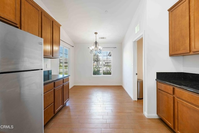 kitchen with visible vents, brown cabinets, light wood-style flooring, freestanding refrigerator, and lofted ceiling