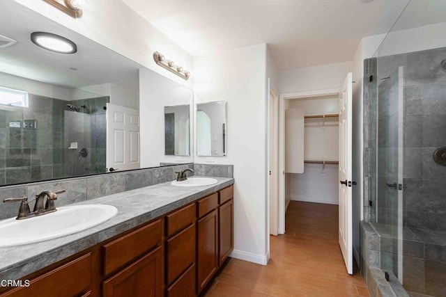 bathroom with a spacious closet, a shower stall, wood finished floors, and a sink