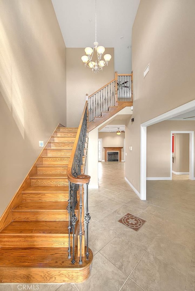 staircase with an inviting chandelier, a fireplace, baseboards, and a towering ceiling