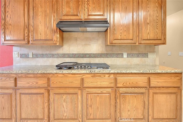 kitchen with under cabinet range hood, light stone countertops, tasteful backsplash, and stainless steel gas stovetop