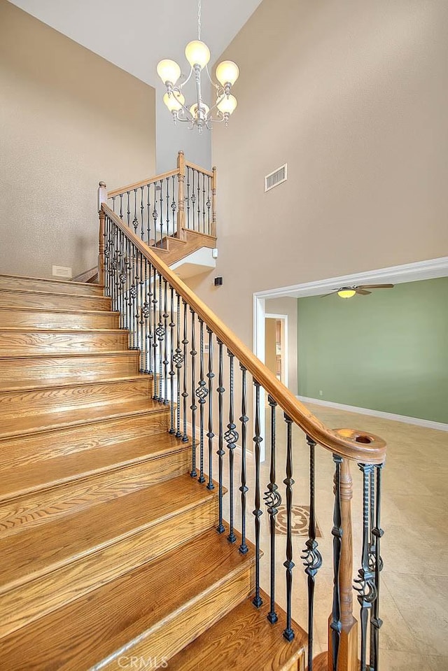 stairway featuring an inviting chandelier, baseboards, visible vents, and a towering ceiling