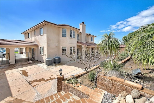 rear view of house with fence, stucco siding, a chimney, a patio, and a gate