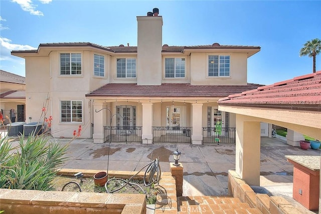 rear view of property featuring a patio area, stucco siding, a chimney, and fence