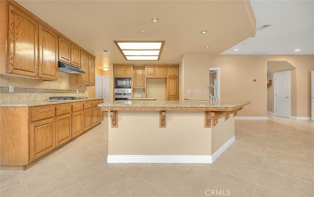 kitchen with a breakfast bar, under cabinet range hood, backsplash, appliances with stainless steel finishes, and light tile patterned floors