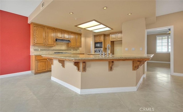 kitchen featuring visible vents, a kitchen bar, under cabinet range hood, backsplash, and black microwave