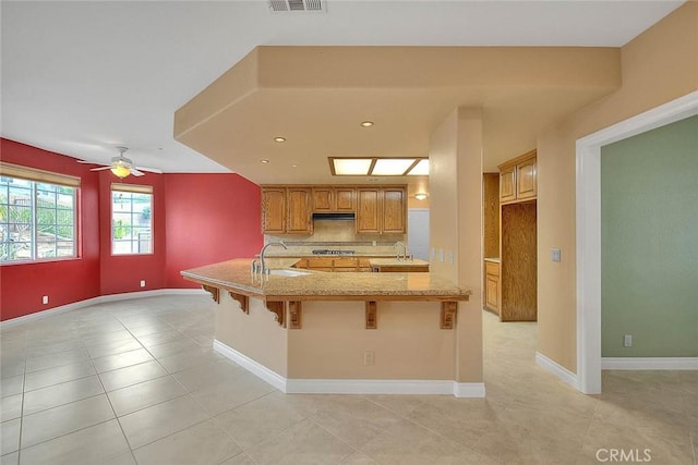 kitchen with under cabinet range hood, stainless steel gas cooktop, a kitchen bar, and a sink