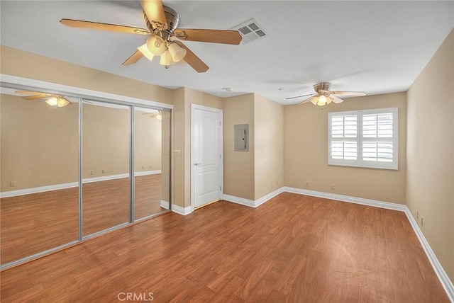 unfurnished bedroom featuring electric panel, wood finished floors, a closet, baseboards, and ceiling fan