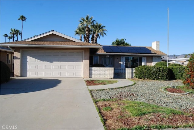 ranch-style house with stucco siding, driveway, roof mounted solar panels, an attached garage, and a chimney