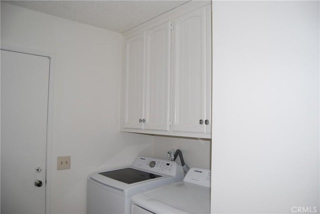 clothes washing area with washer and dryer, cabinet space, and a textured ceiling