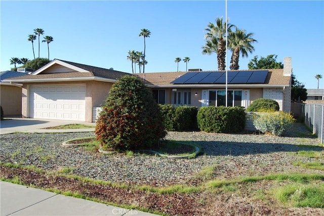 ranch-style house with solar panels, concrete driveway, an attached garage, and fence