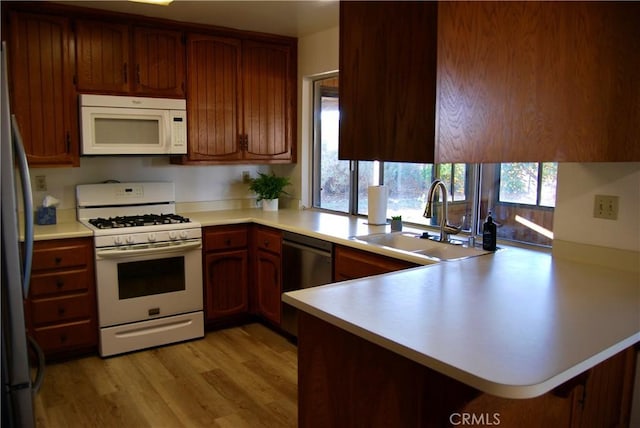 kitchen featuring light countertops, light wood-style flooring, a peninsula, stainless steel appliances, and a sink