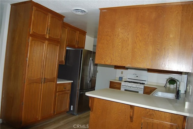 kitchen with visible vents, white range with gas cooktop, brown cabinets, a sink, and freestanding refrigerator