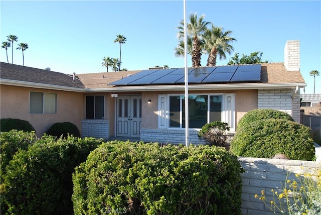 rear view of property with brick siding, solar panels, a chimney, and stucco siding