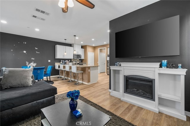 living area with recessed lighting, visible vents, a glass covered fireplace, and light wood finished floors