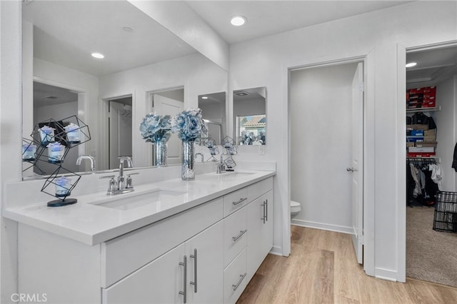 full bath with double vanity, toilet, wood finished floors, and a sink