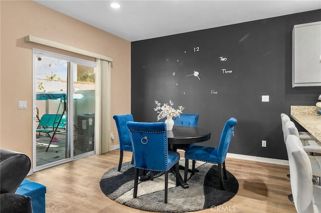 dining room featuring light wood-type flooring, baseboards, and an accent wall