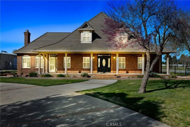 view of front facade with brick siding, a porch, a front lawn, and fence