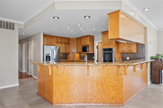 kitchen featuring ornamental molding, appliances with stainless steel finishes, a breakfast bar area, a peninsula, and light stone countertops