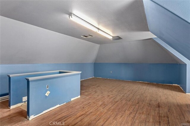 additional living space featuring visible vents, a textured ceiling, wood finished floors, and vaulted ceiling