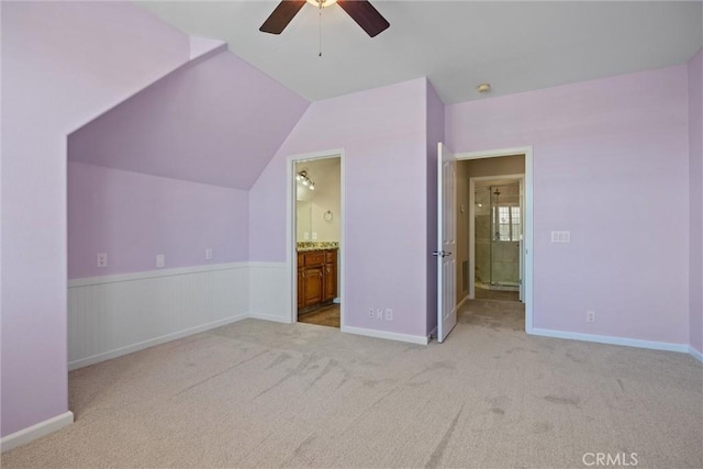 unfurnished bedroom featuring a wainscoted wall, ensuite bath, lofted ceiling, ceiling fan, and carpet flooring