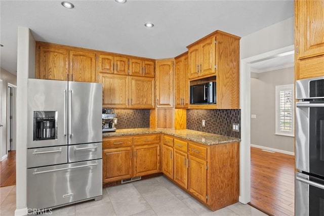 kitchen with light stone counters, brown cabinetry, backsplash, and stainless steel appliances