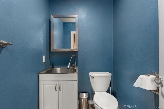 half bathroom with vanity, toilet, and a textured wall