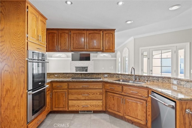 kitchen with ornamental molding, a sink, light stone counters, stainless steel appliances, and brown cabinetry