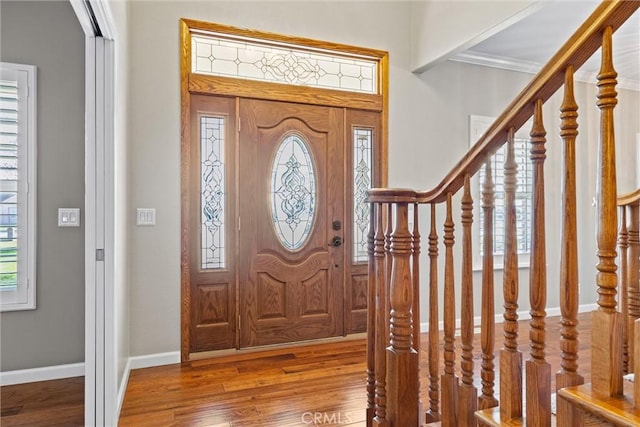 foyer entrance with crown molding, stairs, baseboards, and wood finished floors