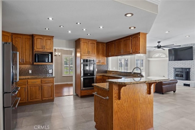 kitchen featuring brown cabinets, a kitchen breakfast bar, open floor plan, stainless steel appliances, and ceiling fan